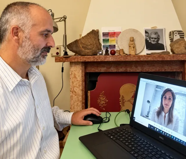 Iuri at his desk during an online video session, with family photographs and keepsakes on the mantelpiece behind him